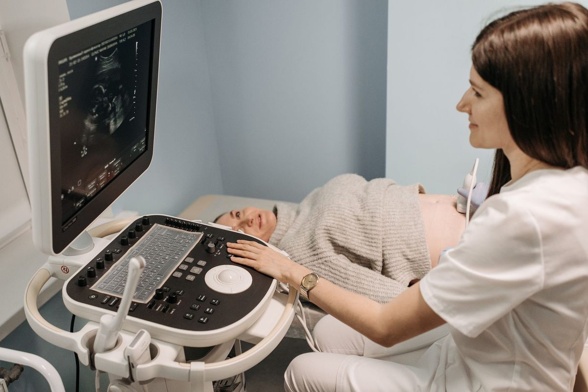 Médica realizando um exame de ultrassom em uma paciente deitada, com o monitor do aparelho ao lado